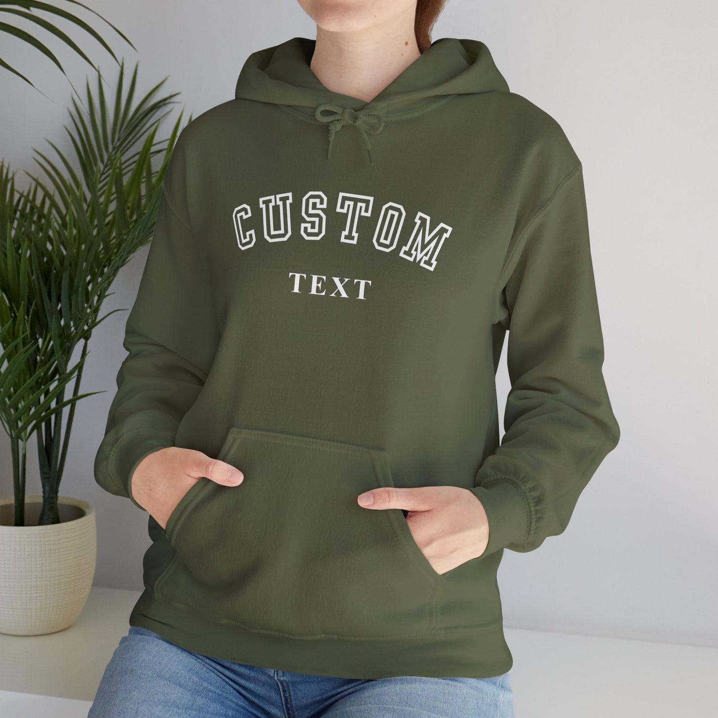 Person wearing a green hoodie with 'CUSTOM TEXT' printed on it, standing indoors next to a plant.