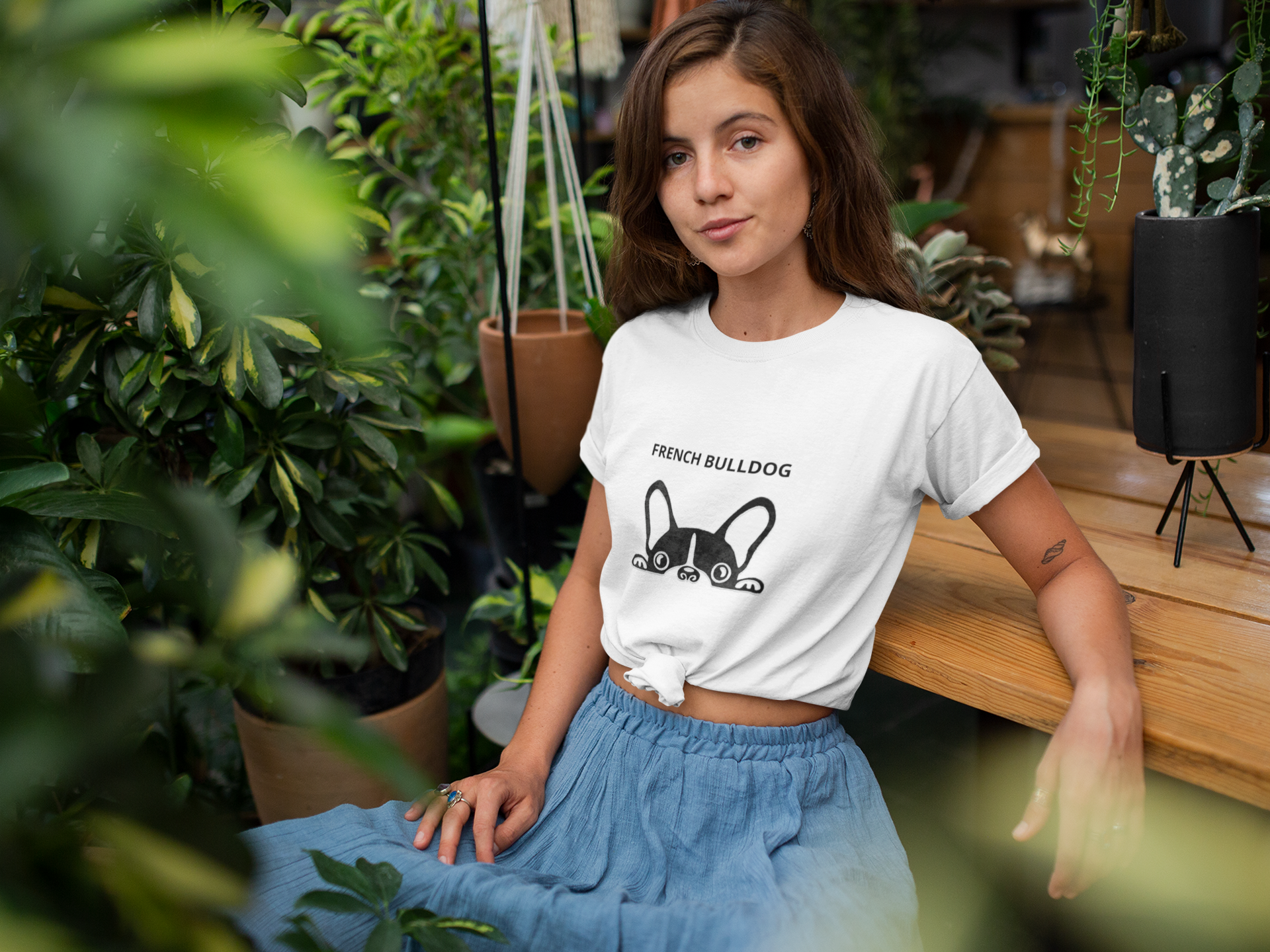 Woman wearing a white t-shirt with a dog graphic in an indoor setting with plants.